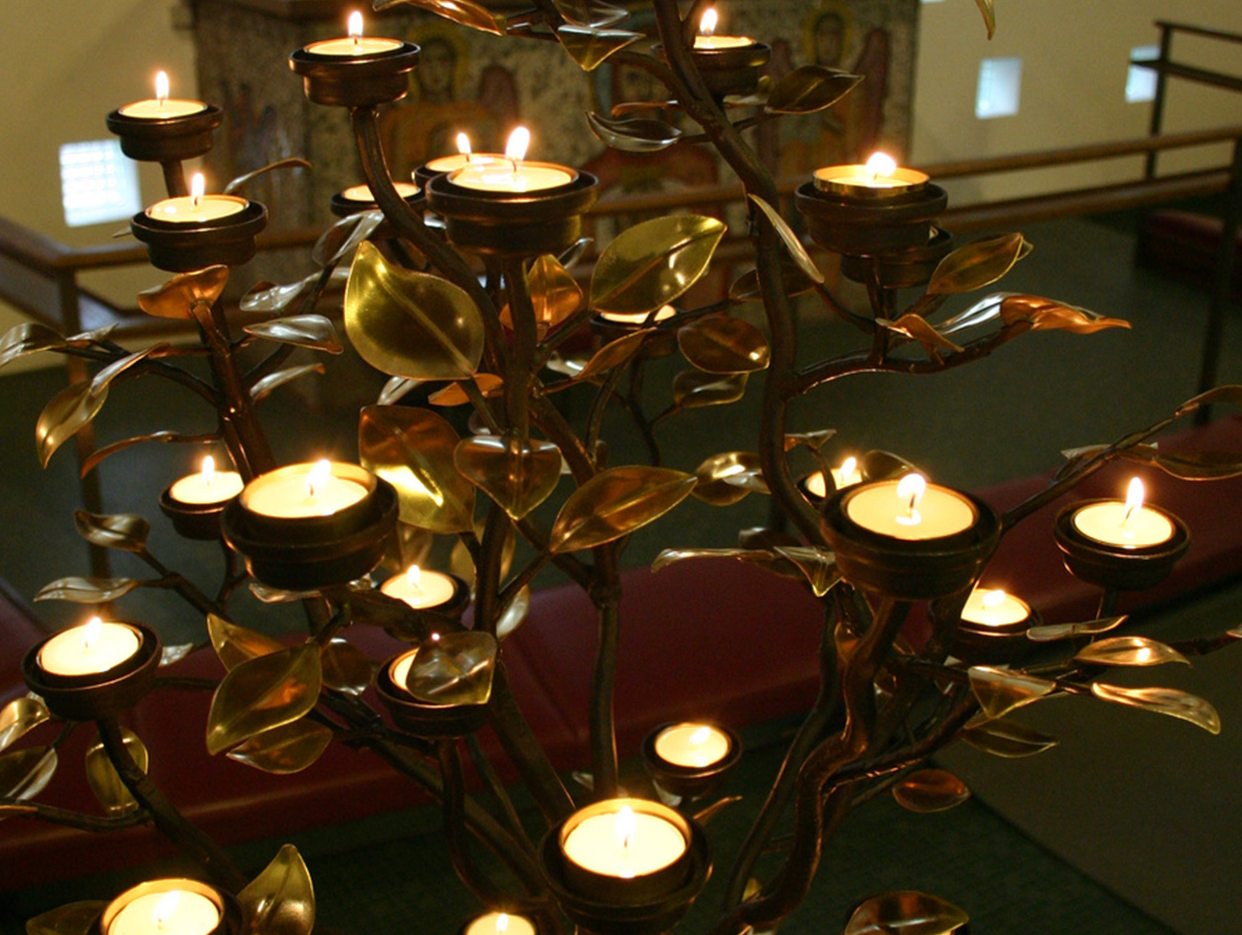 Baumförmiger Kerzenständer aus Metall mit brennenden Teelichtern in einer Kirche.