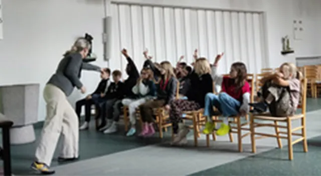 En lærer underviser en klasse af børn, der rækker hænderne op i et klasseværelse.