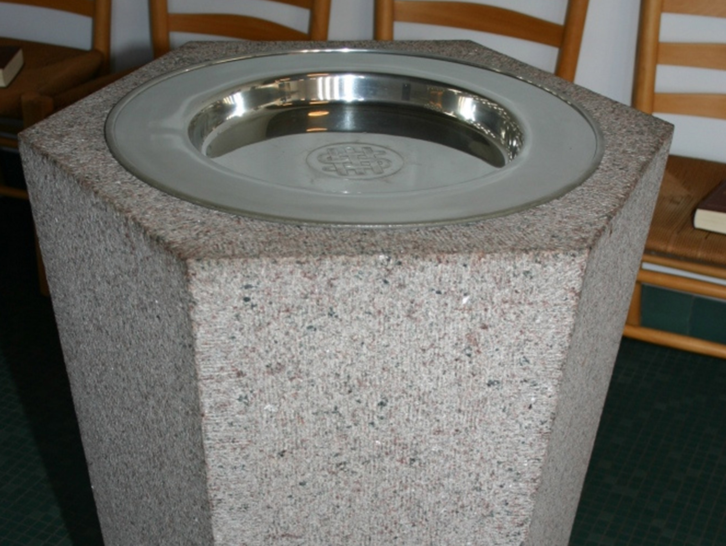 Sechseckiges Taufbecken aus Stein mit einer Silberschale in einer Kirche.