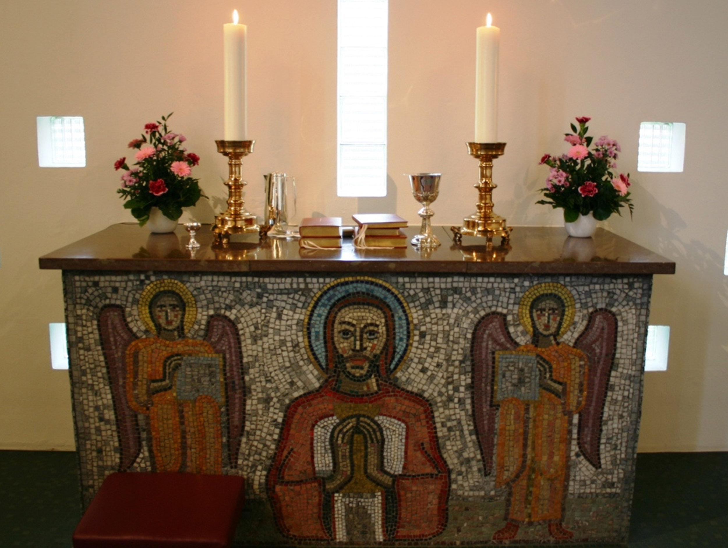 Kirchenaltar, dekoriert mit Kerzen, Blumen und einer Mosaik-Vorderseite mit Christus und Engeln.