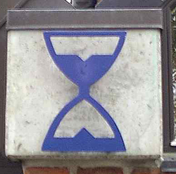 Et blåt timeglas-symbol monteret på en murstensvæg.