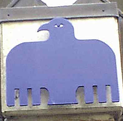 Et blåt ørn-symbol (Johannesevangeliet) monteret på en murstensvæg.