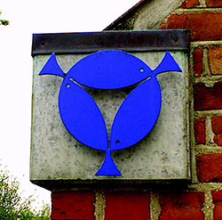Et blåt tre-fisk symbol i en cirkel på en murstensvæg.