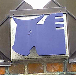 Et blåt vinget okse-symbol (Lukasevangeliet/Zakarias' offer) monteret på en murstensvæg.