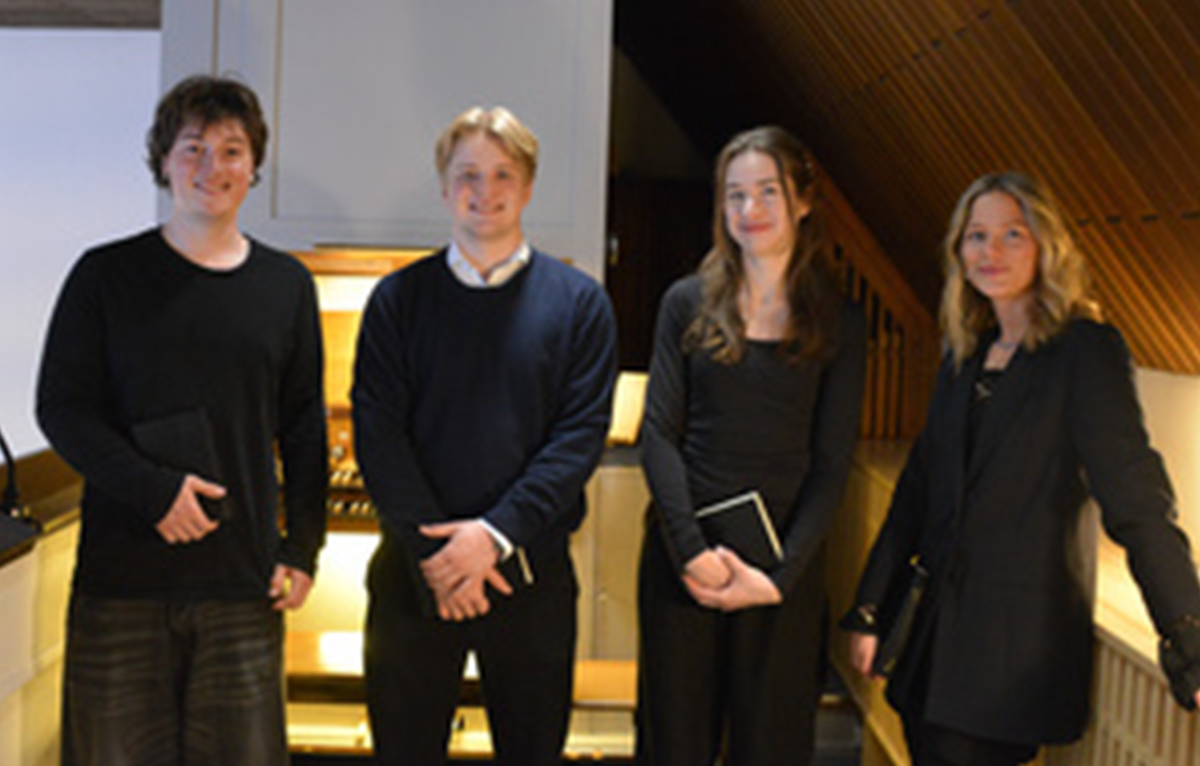 Vier junge Musiker stehen mit Notenbüchern vor einer Kirchenorgel.