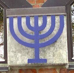 Et blåt syvarmet lysestage-symbol (menora) monteret på en murstensvæg.