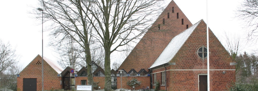 En moderne kirke i røde mursten set udefra med træer i baggrunden.